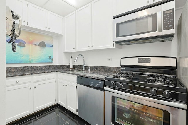 kitchen with stainless steel appliances, a sink, white cabinets, and dark tile patterned flooring