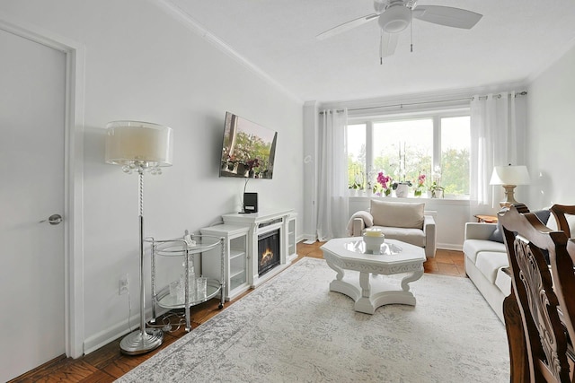 living room featuring ornamental molding, a ceiling fan, baseboards, and a glass covered fireplace