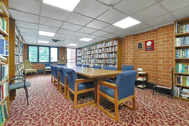 carpeted dining area with a drop ceiling and brick wall