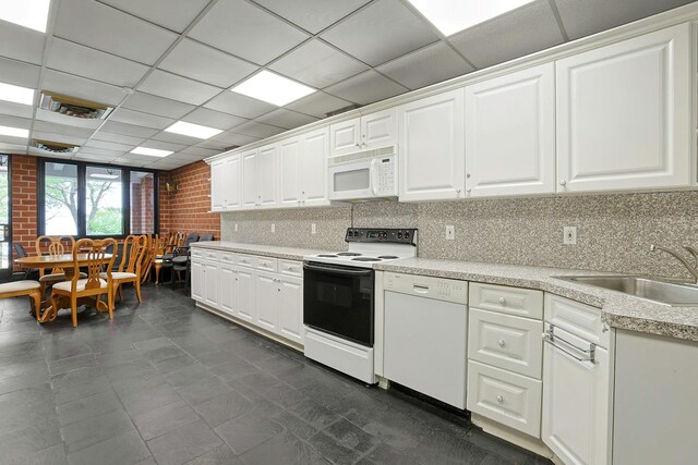 kitchen with white appliances, a drop ceiling, a sink, light countertops, and white cabinets