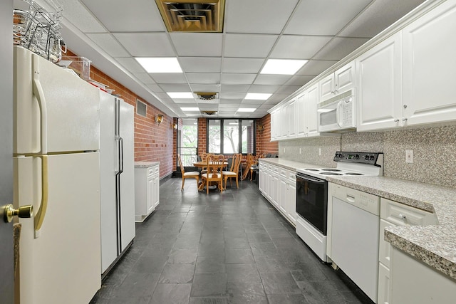 kitchen featuring white appliances, white cabinetry, light countertops, a drop ceiling, and brick wall