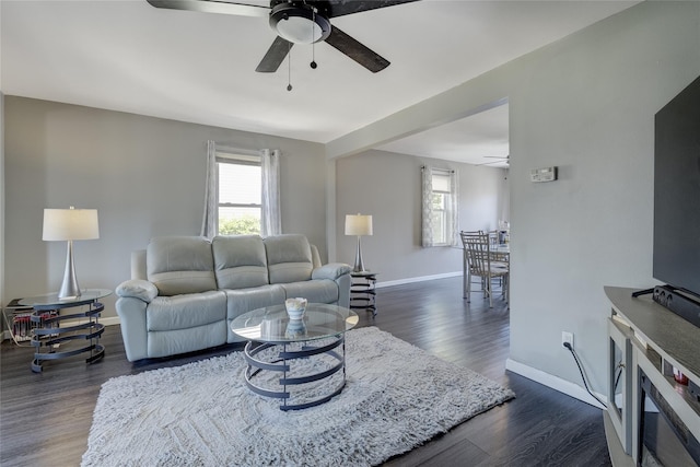 living room featuring a ceiling fan, baseboards, and dark wood-type flooring