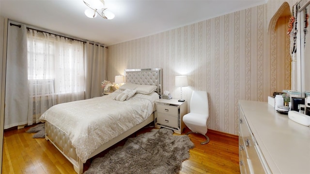 bedroom featuring baseboards, light wood finished floors, wallpapered walls, and arched walkways
