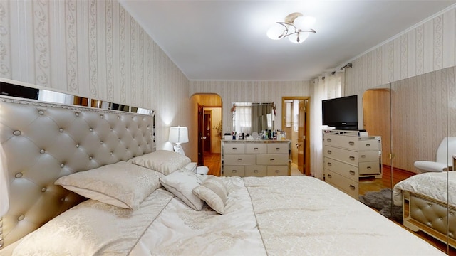 bedroom with arched walkways, connected bathroom, wallpapered walls, and wood finished floors