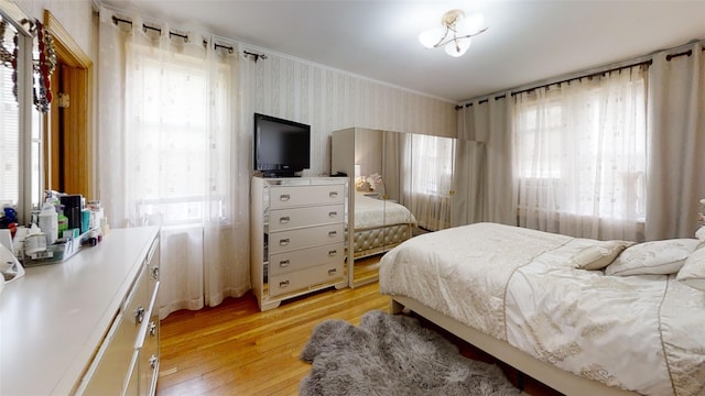 bedroom with crown molding, light wood-style flooring, wallpapered walls, and multiple windows