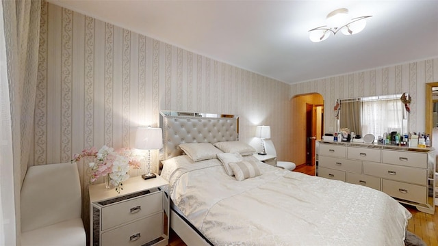 bedroom with wallpapered walls, wood finished floors, and arched walkways