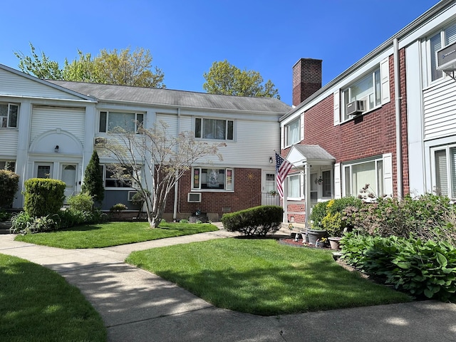 view of property featuring a chimney, brick siding, and a front yard