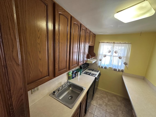 kitchen with a sink, gas range oven, exhaust hood, light countertops, and baseboards