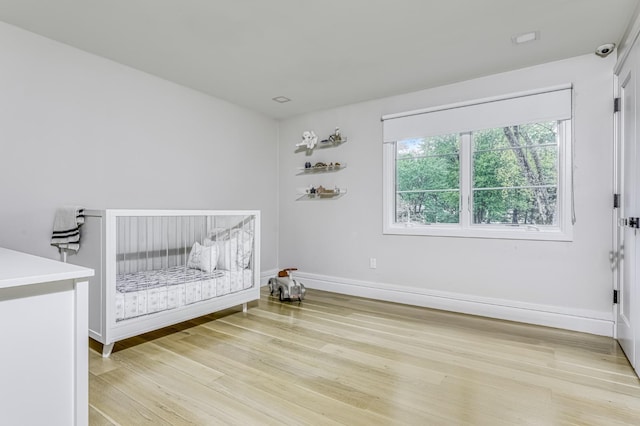 bedroom featuring light wood-style flooring, baseboards, and a nursery area