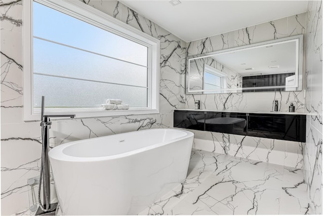 full bathroom featuring marble tiled floors, a freestanding bath, double vanity, and tile walls