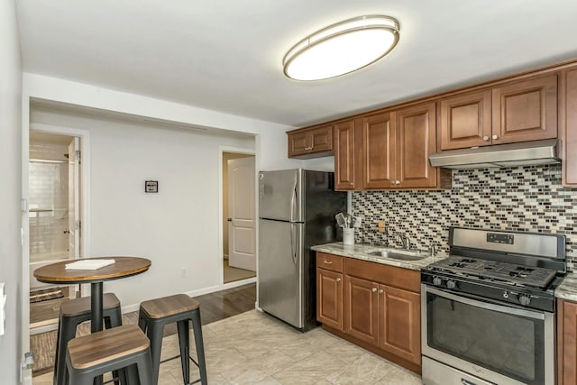 kitchen with stainless steel appliances, a sink, under cabinet range hood, and tasteful backsplash