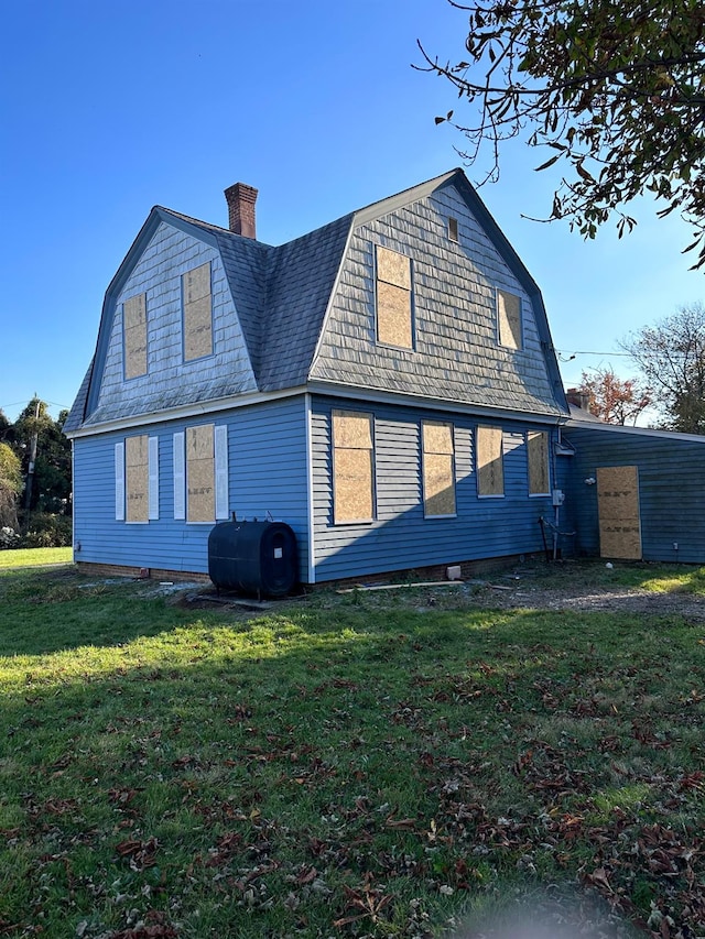 rear view of house featuring a gambrel roof, a chimney, heating fuel, and a lawn