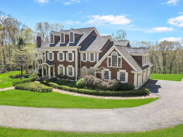 colonial home with an attached garage, driveway, a chimney, and a front lawn