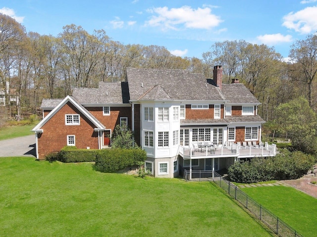back of property with fence, a wooden deck, a chimney, and a lawn