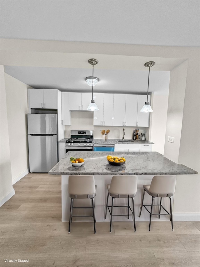 kitchen featuring baseboards, light wood finished floors, a sink, white cabinetry, and stainless steel appliances