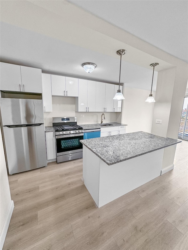 kitchen featuring pendant lighting, light wood finished floors, a sink, white cabinetry, and stainless steel appliances