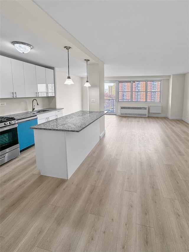 kitchen featuring light wood-style flooring, open floor plan, white cabinetry, stainless steel range with gas cooktop, and radiator heating unit