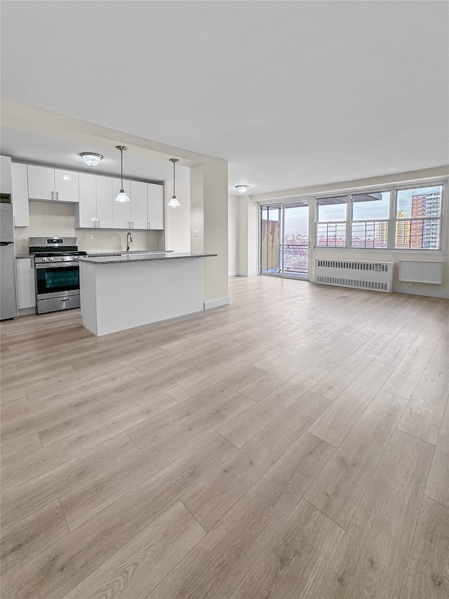 kitchen with radiator heating unit, light wood-style flooring, white cabinetry, open floor plan, and appliances with stainless steel finishes