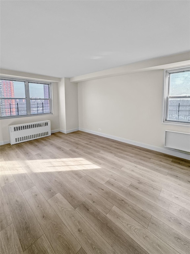 unfurnished room featuring baseboards, radiator heating unit, and wood finished floors