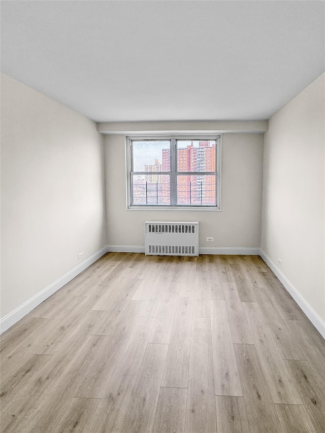 unfurnished room with baseboards, radiator heating unit, and wood finished floors