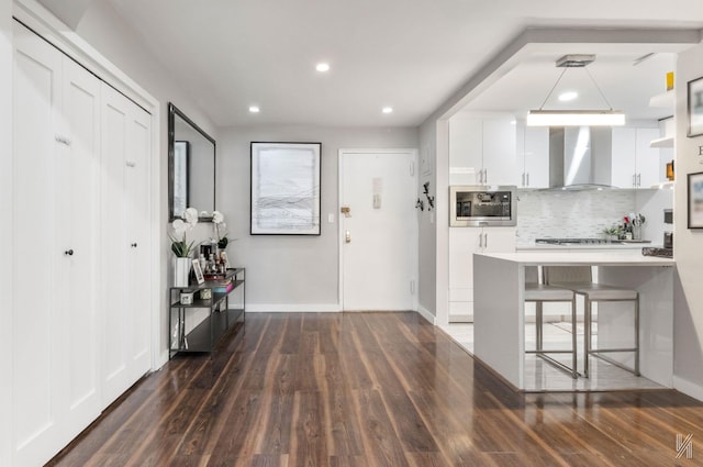 kitchen featuring wall chimney exhaust hood, appliances with stainless steel finishes, white cabinetry, tasteful backsplash, and dark wood-style floors