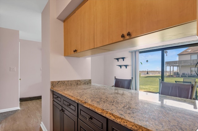 kitchen featuring light stone countertops, light wood-type flooring, and baseboards