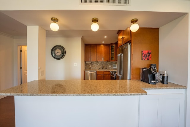 kitchen with stainless steel appliances, brown cabinetry, ornamental molding, backsplash, and a peninsula