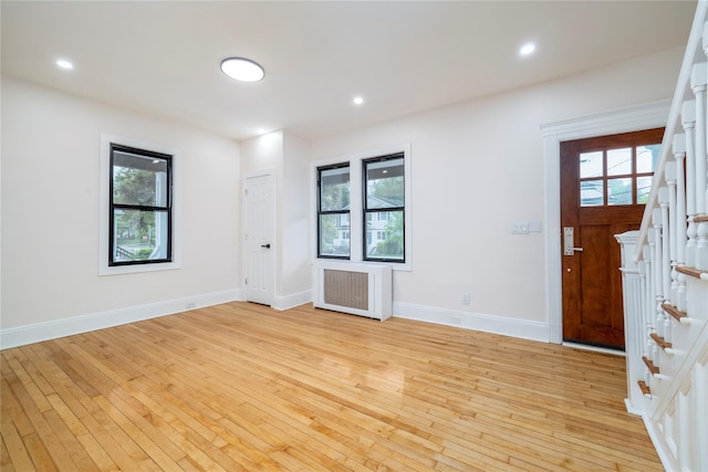 entrance foyer with radiator, stairway, a healthy amount of sunlight, and light wood finished floors
