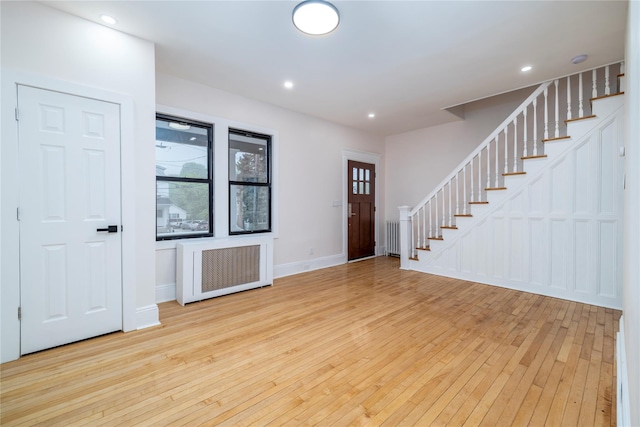 foyer entrance with stairs, radiator, baseboards, and light wood-style floors