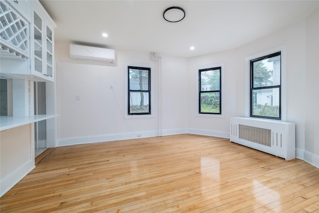 empty room with light wood-type flooring, radiator, a wall unit AC, and a wealth of natural light