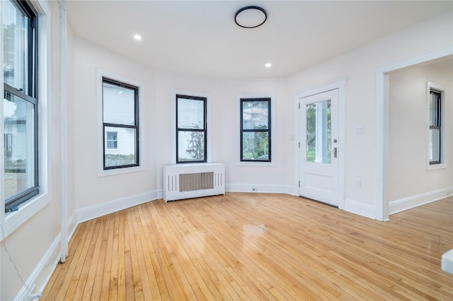 empty room with radiator, light wood-style flooring, baseboards, and recessed lighting