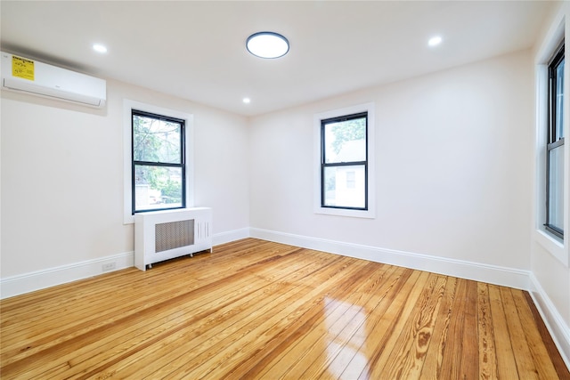 spare room with a wall mounted air conditioner, light wood-style floors, baseboards, and radiator heating unit