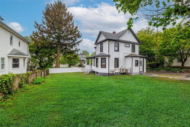 rear view of property featuring a yard, fence, and a shingled roof