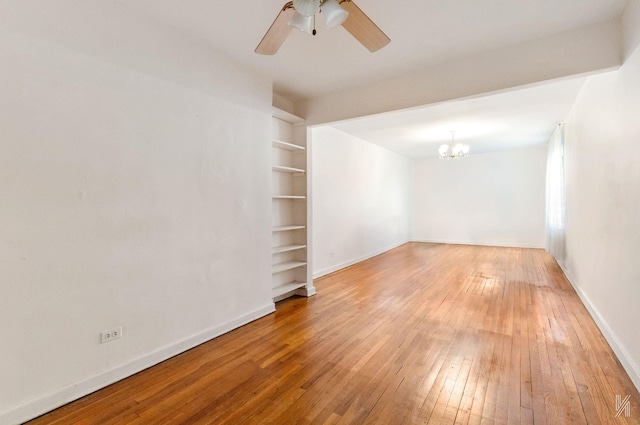 spare room with a chandelier, hardwood / wood-style flooring, ceiling fan, baseboards, and built in shelves