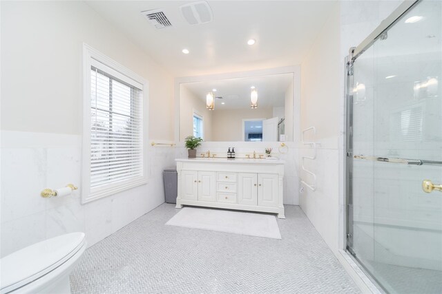 full bathroom featuring tile walls, a stall shower, wainscoting, double vanity, and toilet