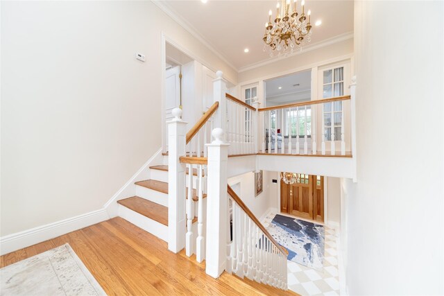 staircase with wood finished floors, a chandelier, ornamental molding, and recessed lighting