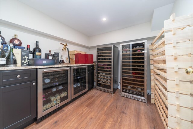 wine area with wine cooler, a bar, wood finished floors, and recessed lighting