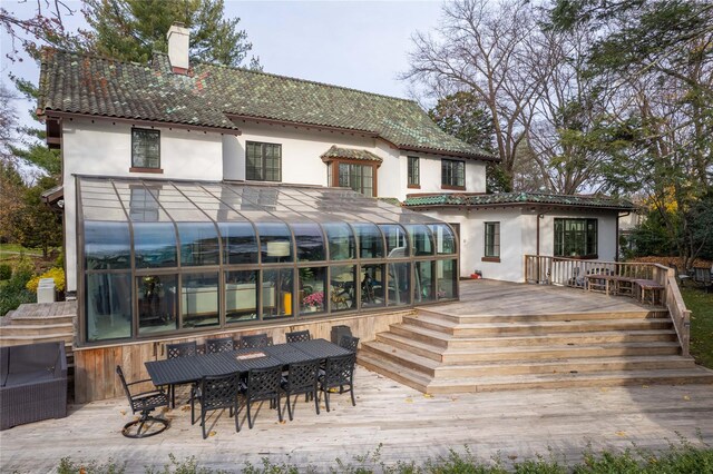 back of house featuring a wooden deck, stucco siding, a sunroom, a chimney, and outdoor dining space