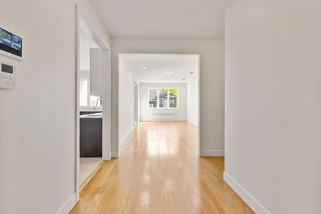 hall with radiator heating unit, light wood-type flooring, and baseboards