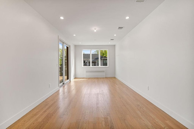 spare room with radiator heating unit, light wood-type flooring, baseboards, and recessed lighting
