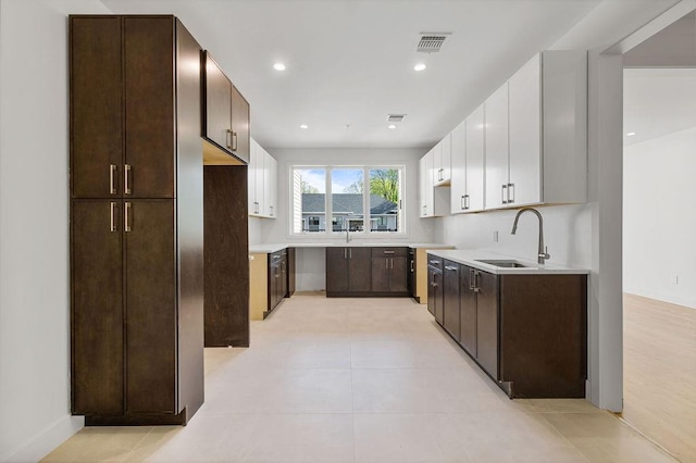 kitchen featuring a sink, dark brown cabinets, white cabinets, light countertops, and recessed lighting