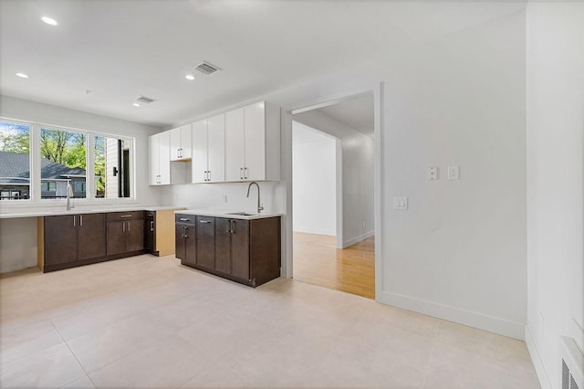 kitchen featuring dark brown cabinetry, light countertops, white cabinetry, a sink, and recessed lighting
