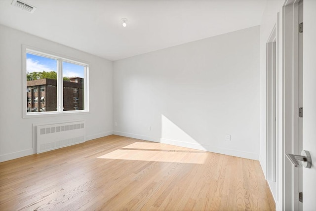 empty room with radiator, light wood finished floors, and baseboards
