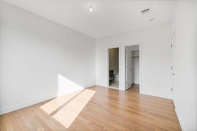 unfurnished bedroom featuring light wood finished floors, baseboards, and a walk in closet