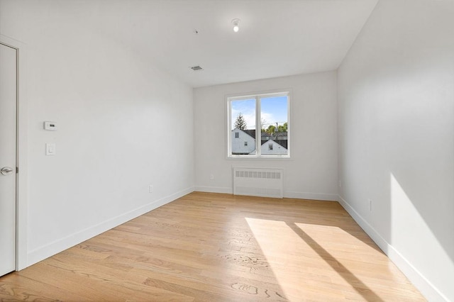 empty room featuring radiator, light wood-style flooring, and baseboards