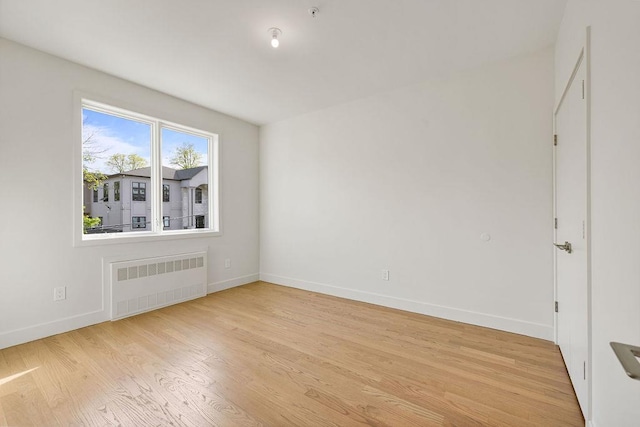 unfurnished room with radiator, baseboards, light wood-type flooring, and fire sprinkler in ceiling