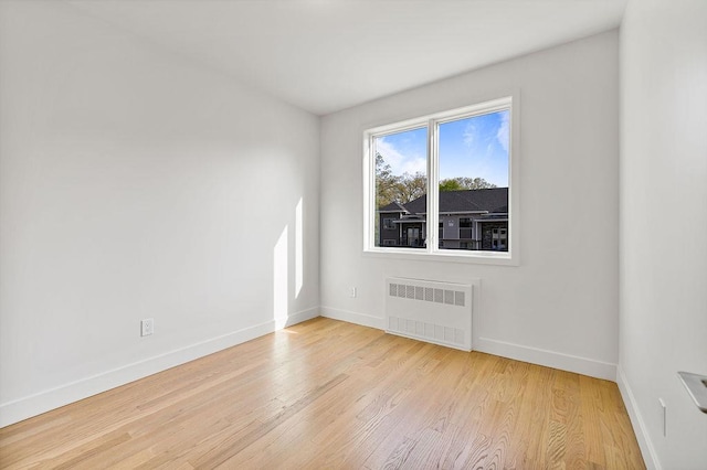 spare room with radiator heating unit, baseboards, and wood finished floors