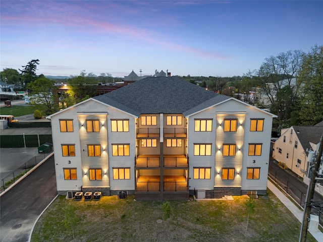 back of property at dusk with fence, a balcony, central AC, and roof with shingles