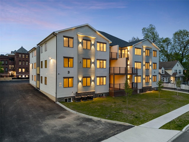 back of property with central air condition unit, a lawn, and a balcony