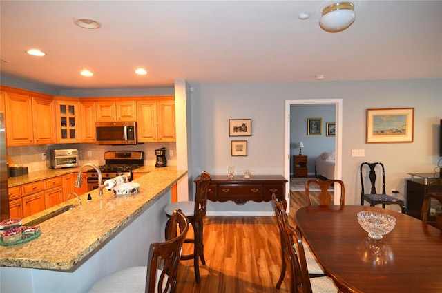 1308 Round Pointe Dr Unit 1308, Haverstraw, NY 10927 - kitchen featuring appliances with stainless steel finishes, a kitchen bar, wood finished floors, light stone countertops, and glass insert cabinets